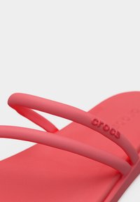 Ροζ σαγιονάρα της μάρκας Crocs με δύο λεπτά λουράκια, υφασμένο πέλμα και ανάγλυφο λογότυπο "crocs" στο πάνω λουράκι.