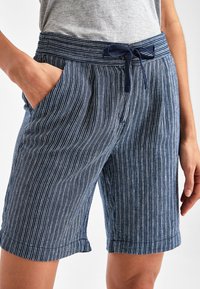 Granatowe, pasiasty szorty wykonane z lekkiego materiału. Posiadają elastyczny pas z troczkiem oraz boczne kieszenie. Wywinięte mankiety.