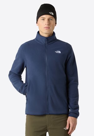 Marineblauwe fleece jas met een hoge kraag, een ritssluiting aan de voorkant en twee zijzakken. Bevat het logo aan de bovenkant aan de linkerkant. Zwarte beanie.