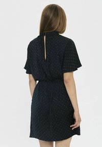 Vestido azul marino con mangas cortas tipo volantito, con lunares blancos, cinturilla ceñida y un detalle de ojal en la parte posterior.