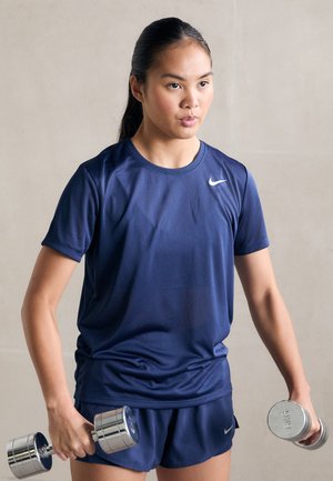 T-shirt et shorts de sport navy en tissu lisse. La personne tient des haltères chromés. Logo Nike sur la poitrine du T-shirt.
