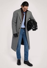 Šedý vlněný kabát s klopami s výstřihem, hnědá kožená podšívka, modrá pruhovaná košile, džínové kalhoty, černé rukavice a černá taška.