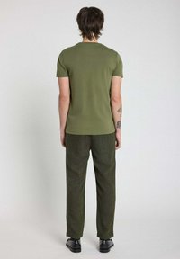 T-shirt à manches courtes vert olive en tissu doux, associé à un pantalon texturé foncé et des chaussures noires, vu de dos.