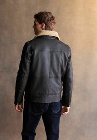 Jachetă din piele neagră cu guler din blană bej, textură matlasată și mâneci cu fermoar. Purtați cu blugi de denim de culoare albastru închis.