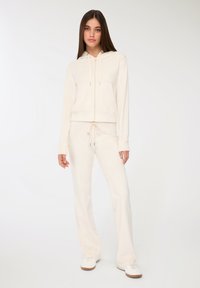 Kremowa hoodie z sznurkiem i kieszenią, zestawiona z pasującymi kremowymi spodniami. Miękka tkanina i luźny krój. Sneakersy dopełniają wygląd.