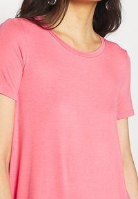 Růžové tričko s krátkým rukávem a kulatým výstřihem, vyrobené z měkké tkaniny, s hladkým povrchem a volným střihem.