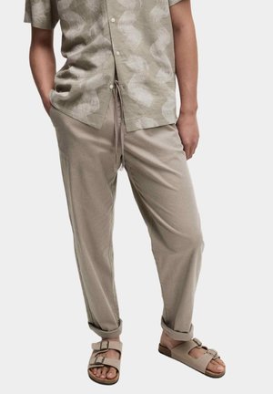 Lichte, short-sleeve shirt in gedempt groen met witte golfpatronen; gecombineerd met beige broek met trekkoord en tan sandalen.