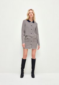 Tvådelat set med ett houndstooth-mönster, som har en kortärmad knäppjacka och en matchande kjol, i kombination med knähöga svarta stövlar.