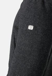 Giacca grigio carbone con tessuto strutturato, con un piccolo logo "Jeanscode" argentato sulla manica e un design strutturato.