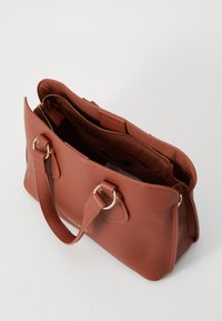 Sac à main en cuir marron texturé avec deux poignées courtes, accents en métal doré, et une fermeture éclair ouverte. L'intérieur est doublé en tissu.
