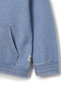 Sudadera de mezclilla azul clara con un solo bolsillo frontal, detalles de costura marrón y una pequeña etiqueta gris con una estrella en el puño de la manga.