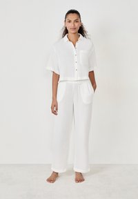 Witte, lichte katoenen loungewear set met een kort065 mouwen knoopshirt en broek met elastische tailleband, met een voorzak en omgeslagen mouwen.