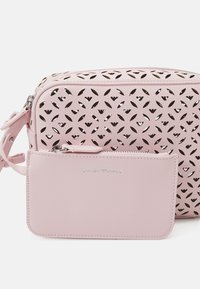 Różowa perforowana torebka o gładkiej fakturze, z odpinanym dopasowanym etui na karty, srebrnymi okuciami oraz kwiatowym wzorem wycinanym w materiale.