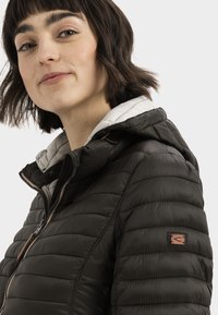 Zwarte pufferjack met capuchon, verticale stiksels, contrasterende witte voering en een klein logopatch op de linker mouw.