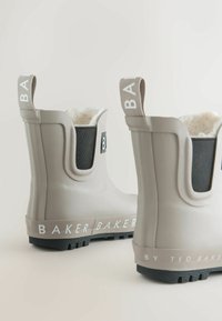 Lichtbeige rubberen enklaarzen met donkere elastische zijpanelen, fleecevoering en "BAKER" bedrukt op de banden. Kenmerken zijn de getextureerde zolen.