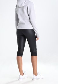 Capris atléticos negros con detalles de malla en las rodillas, combinados con una sudadera gris claro. La tela parece suave y elástica.