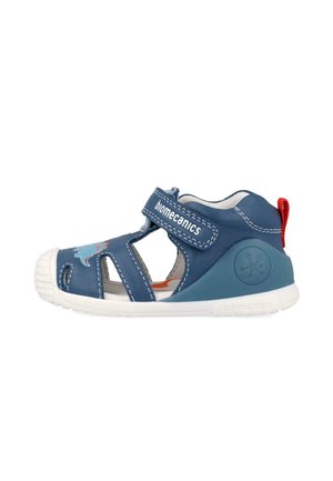 Sandalia azul de cuero para niño pequeño con suela blanca, correa ajustable de velcro etiquetada "biomecanics", diseño de dinosaurio y tirador rojo en el talón.
