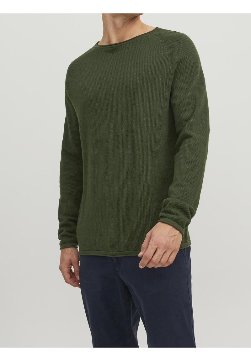 Grön långärmad tröja med en texturerad stickad design, rund halsringning och ribbade ärmslut, ihop med mörka byxor. Inga synliga logotyper eller mönster.