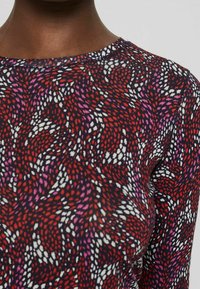 Långärmad topp med ett färgglatt virvelmönster i röd, rosa och vitt på en mörk bakgrund. Standard modell med rund halsringning.