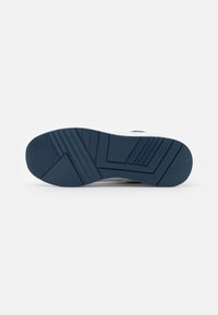 Suela de zapatilla con un material de goma azul texturizado, con surcos diagonales y horizontales, etiquetada con "GUESS" en el lateral.