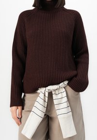 Maglione in maglia a coste color borgogna scuro con collo alto, abbinato a pantaloni beige con cintura regolabile a righe bianche in vita.