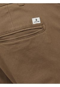 Pantaloni di cotone marrone con una tasca posteriore caratterizzata da un motivo ricamato e una piccola etichetta bianca con testo nero, "JACK&JONES".