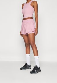 Różowy sportowy top croptop i pasujące szorty z logo Nike. Czarne trampki z teksturowaną podeszwą oraz białe skarpetki z logo Nike.