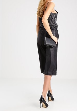 Zwarte culottes van imitatieleer met elastische tailleband; gecombineerd met een gestructureerde grijze top en een zwarte gewatteerde crossbodytas; zwarte hoge hakken.