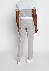 Pantaloni grigi chiari su misura con una texture liscia, abbinati a una camicia a righe a maniche corte in azzurro e bianco. Sneakers bianche visibili.