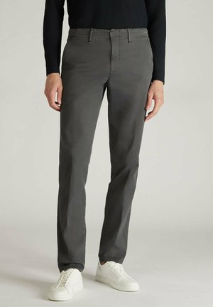 Graue Baumwollhosen mit schmaler Passform, featuring einen Reißverschluss, Gürtelschlaufen und seitlichen Taschen. Kombiniert mit weißen Sneakern auf einem neutralen Hintergrund.