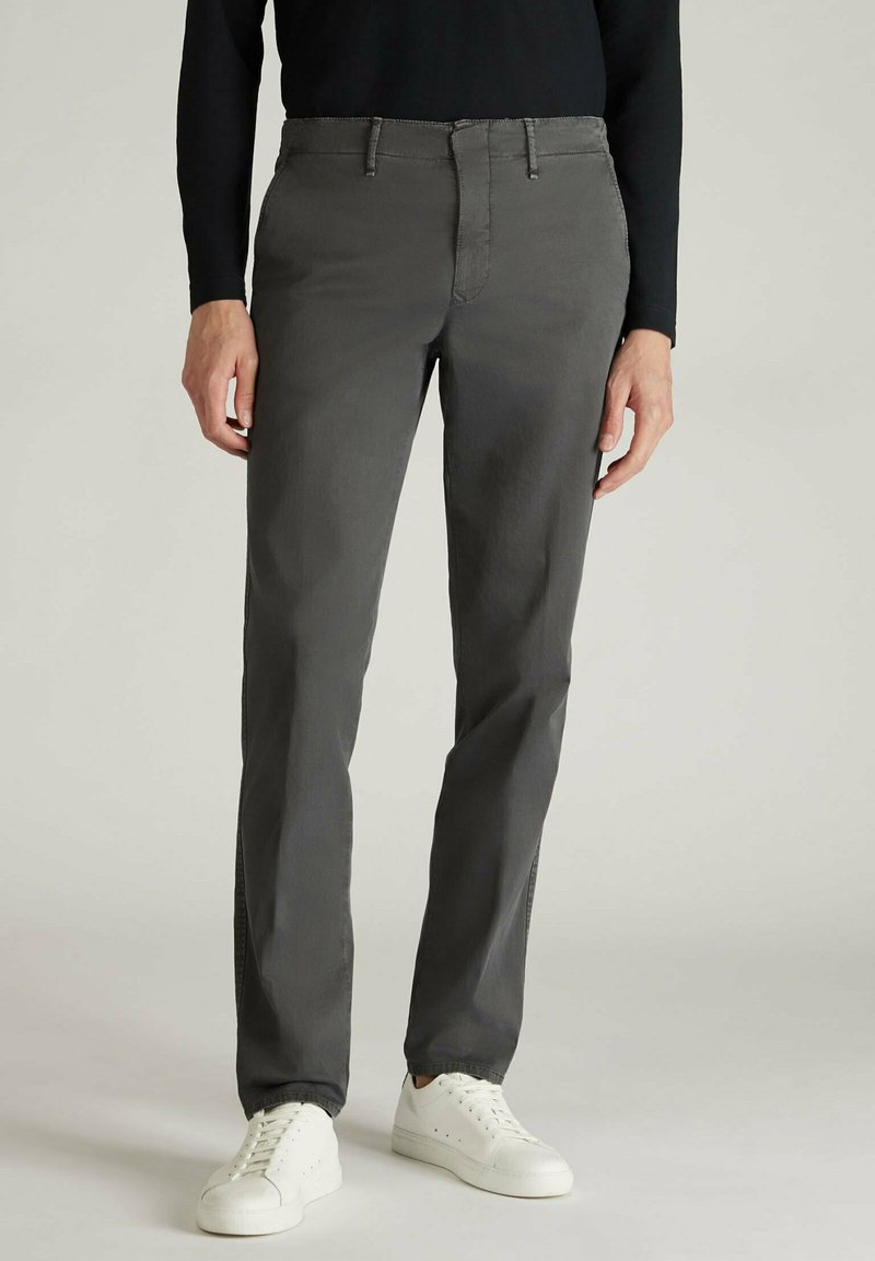 Pantaloni in cotone grigi con una vestibilità slim, dotati di zip sul davanti, passanti per cintura e tasche laterali. Abbinate a sneakers bianche su uno sfondo neutro.
