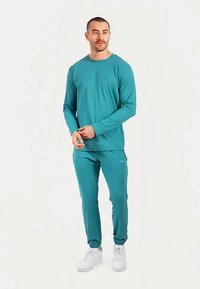 Turquoise top met lange mouwen en bijpassende taps toelopende broek van een soepel, lichtgewicht materiaal. Voorzien van elastische manchetten en een subtiel logo op de broek.