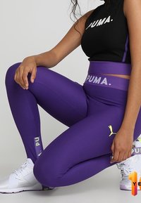 Fioletowe rypsowane legginsy z wysokim stanem, z żółtym logo Pumy. W zestawieniu z czarnym krótkim topem z napisem "PUMA" w białym kolorze.