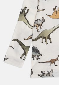 Majica dugih rukava s printom dinosaura u zelenoj, smeđoj i sivoj boji na mekanom bijelom materijalu, s okruglim izrezom i prošivenim rubom.