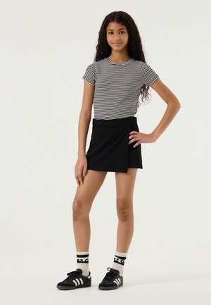 Falda negra cruzada combinada con una camisa de manga corta a rayas verticales. La modelo lleva zapatillas negras y calcetines con estampado.