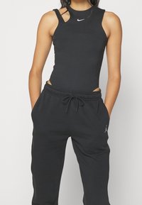 Svart ärmlös topp med utskärningsdesign och en liten vit logotyp. Matchad med svarta joggerbyxor, även med logotyp och dragsko i midjan.