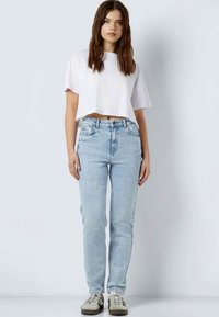 Apkarpytas baltas marškinėlis trumpomis rankovėmis, šviesiai mėlynos džinsinės kelnės ir smėlio spalvos sportbačiai. Paprastas dizainas ir laisvas siluetas neformaliam stiliui.