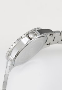 Orologio in acciaio inossidabile argento con una lunetta testurizzata, corona prominente e bracciale segmentato, caratterizzato da una finitura lucida e spazzolata.