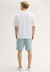 Witte korte mouwen overhemd gedragen met lichtblauwe shorts, met een relaxte pasvorm, en gecombineerd met witte sneakers met een bruine accenten.