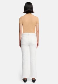 Beige aansluitend T-shirt met korte mouwen en ronde hals, gecombineerd met hooggelegen witte uitlopende jeans, voorzien van Achterzakken en een gladde textuur.