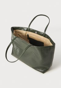 Green woven leather tote bag with two handles, spacious interior, beige lining, and a zippered pocket inside.
