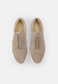 Beige semskinn sneakers med rundet tå, snøresystem, perforerte detaljer og hvite gummisåler. Minimalistisk design.