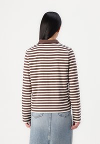 Long-sleeve polo shirt with brown and cream horizontal stripes, features a brown collar, and is paired with a denim skirt.