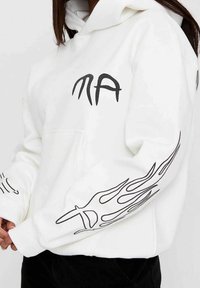 Witte hoodie met zwarte vlamgraphic ontwerpen op de mouwen en de voorkant, met een kangoeroezak en trekkoordkap. Zachte stoftextuur.