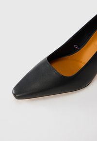 Black pointed-toe leather women's shoe with a low-cut design and tan cushioned insole on white background.