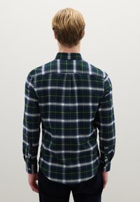 Camicia a quadri con schema di colori blu e verde, con accenti bianchi e gialli. Il materiale è morbido con maniche lunghe e polsini con bottoni.