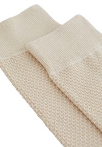 Bézs színű, textúrázott zoknik bordázott felső résszel és szövéssel díszített testtel, melyek lágy tapintásúak és meleg színárnyalatokkal rendelkeznek.