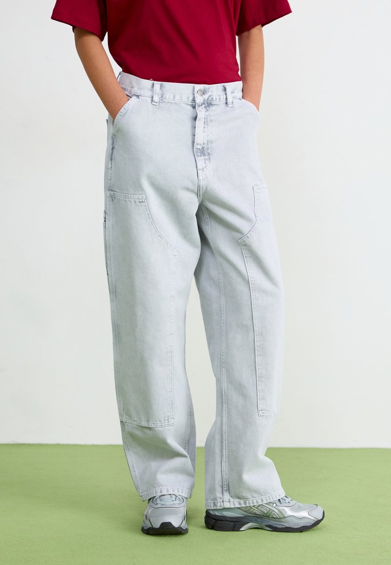 Jeans in denim azzurro chiaro a gamba larga con vita alta, dotati di tasche anteriori e posteriori. Abbinati a una maglietta rossa a maniche corte e sneaker grigie.