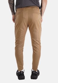 Pantalones acampanados color beige con cinturilla elástica, dos bolsillos traseros y bolsillos laterales con cremallera. El material parece suave y ligero.