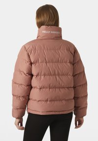 Light pink puffer jacket with horizontal quilted segments. High collar features “HELly HANSEN” logo in white. Material appears soft and insulated.
